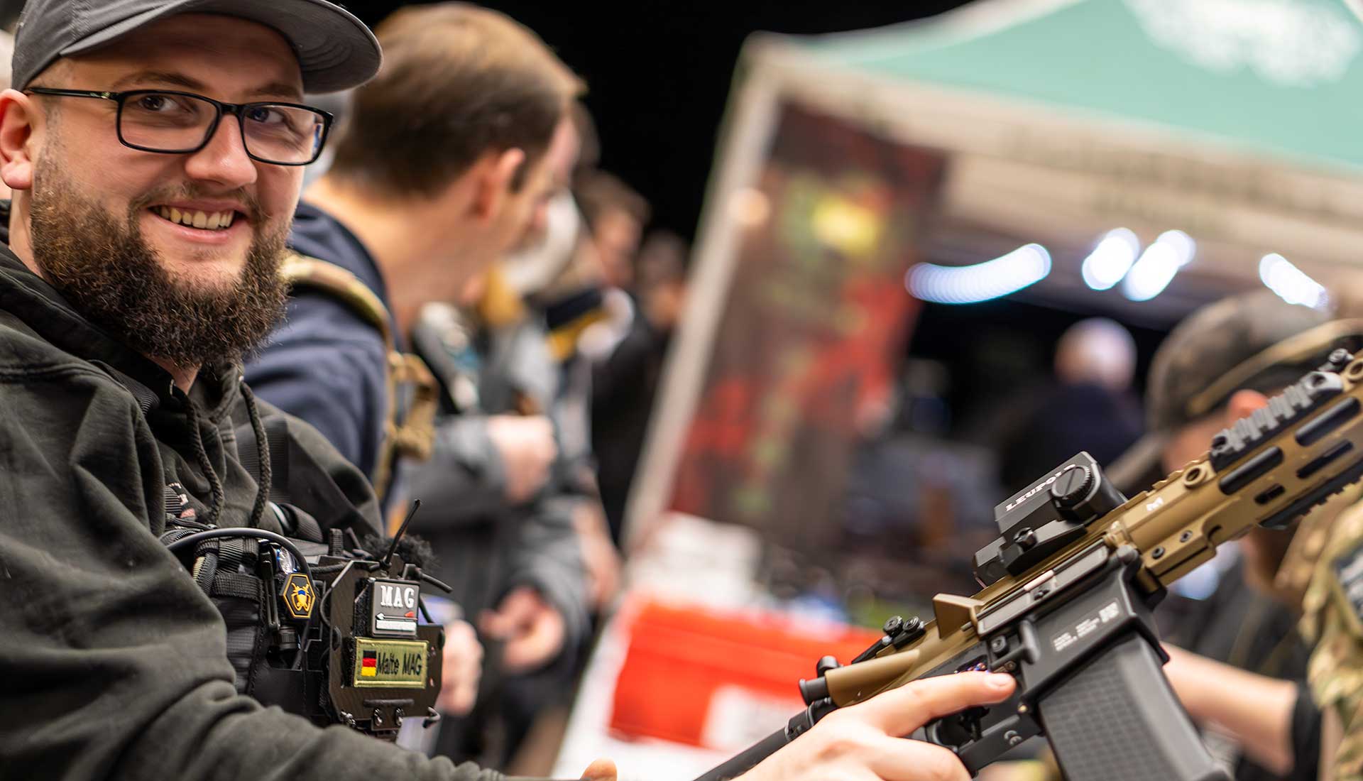 sw-startseite-slider Ein junger Mann lächelt in die Kamera und hält ein Airsoft-Gewehr in der hand
